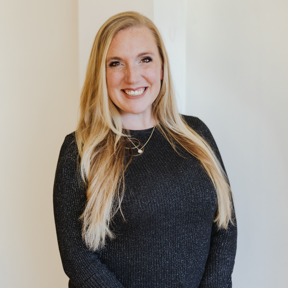 Person standing in front of a white wall and smiling.