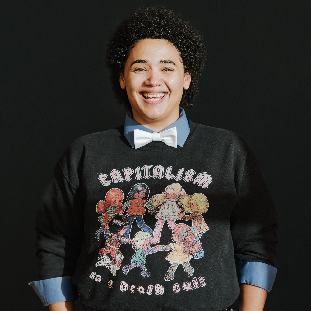 Person in a t-shirt and bow tie smiling.