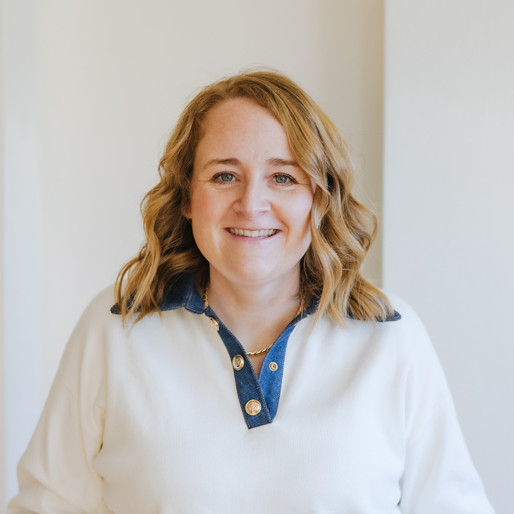 Person in a white sweater smiling against a white background.