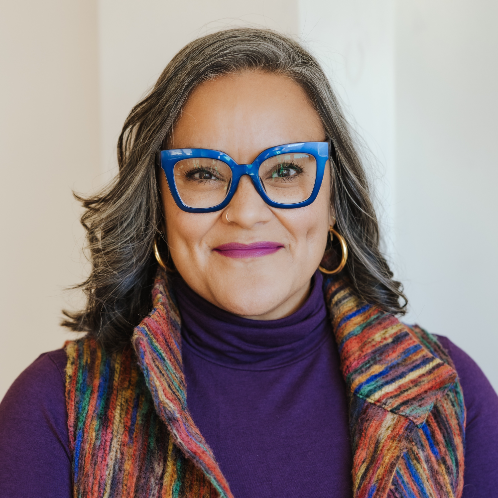 Person wearing blue glasses and a bold vest smiling.