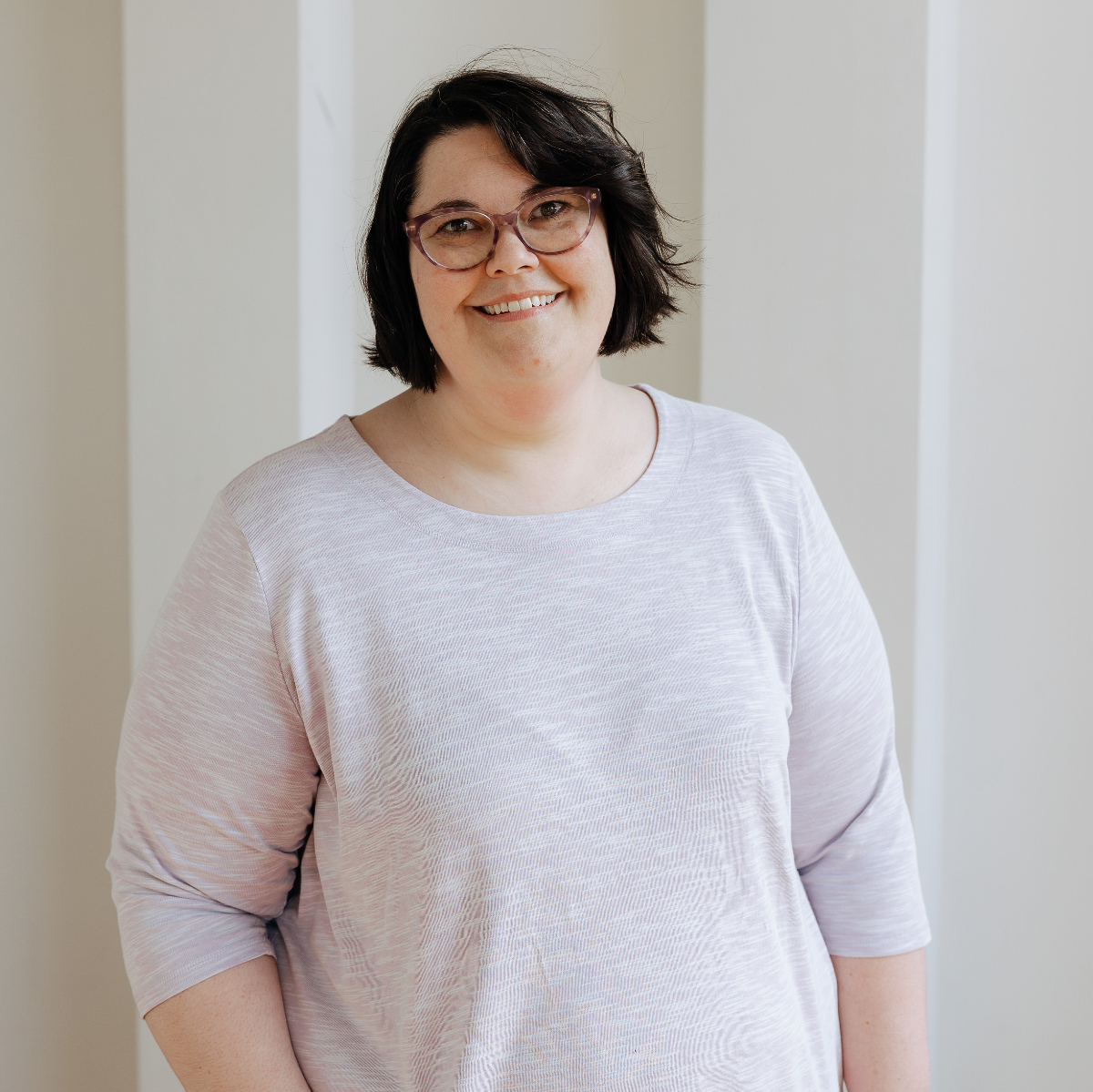 Person in a light colored sweater standing and smiling at the camera.