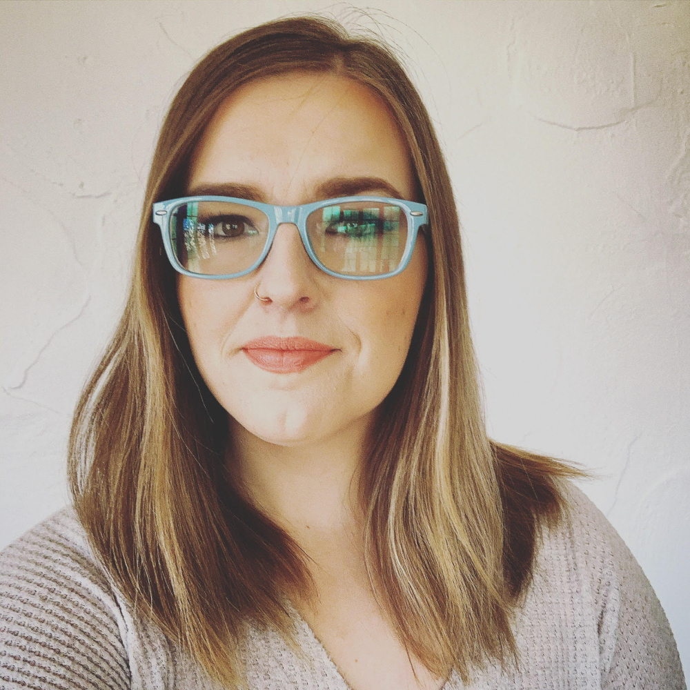 Person wearing green glasses smiling slightly.